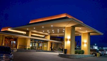 A well-lit building with a covered entrance at night, featuring modern architecture and a few cars parked outside.