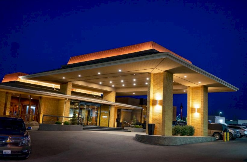 A well-lit building with a covered entrance at night, featuring modern architecture and a few cars parked outside.