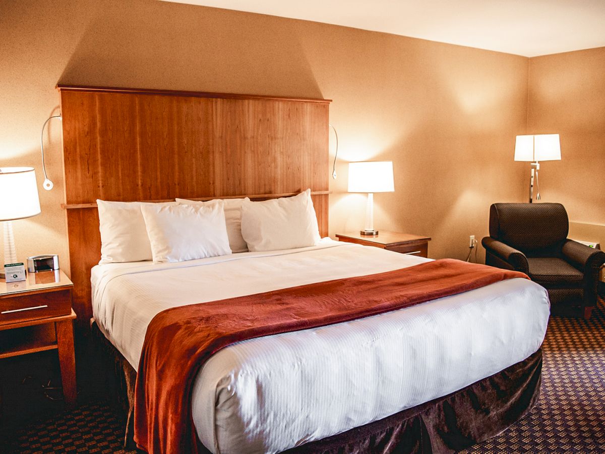 A cozy hotel room with a large bed, bedside tables with lamps, a dark armchair, and warm lighting, creating a welcoming and comfortable atmosphere.