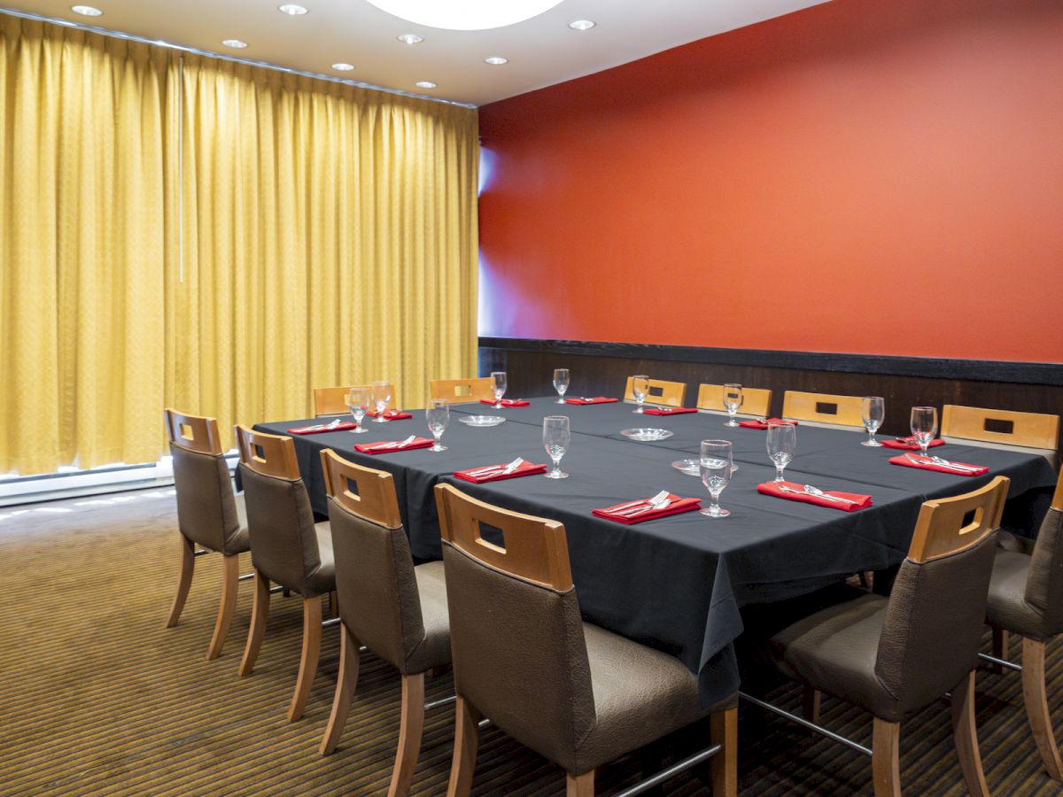 A conference room with a black tablecloth, set for a meeting with glasses and red napkins, surrounded by chairs, yellow drapes partly closed.