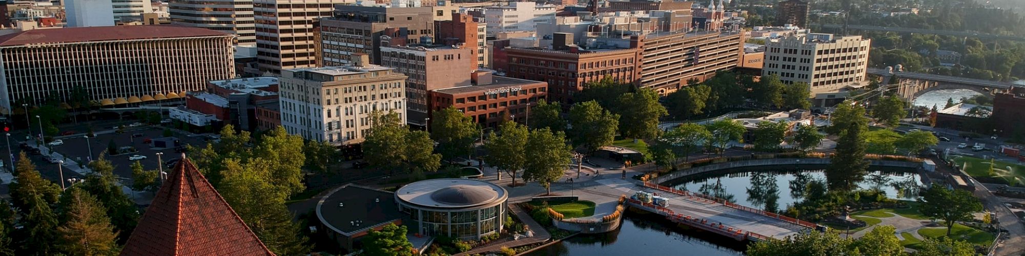 The image shows a cityscape with a prominent clock tower, several buildings, and a park area with a pond and greenery, creating a tranquil urban scene.