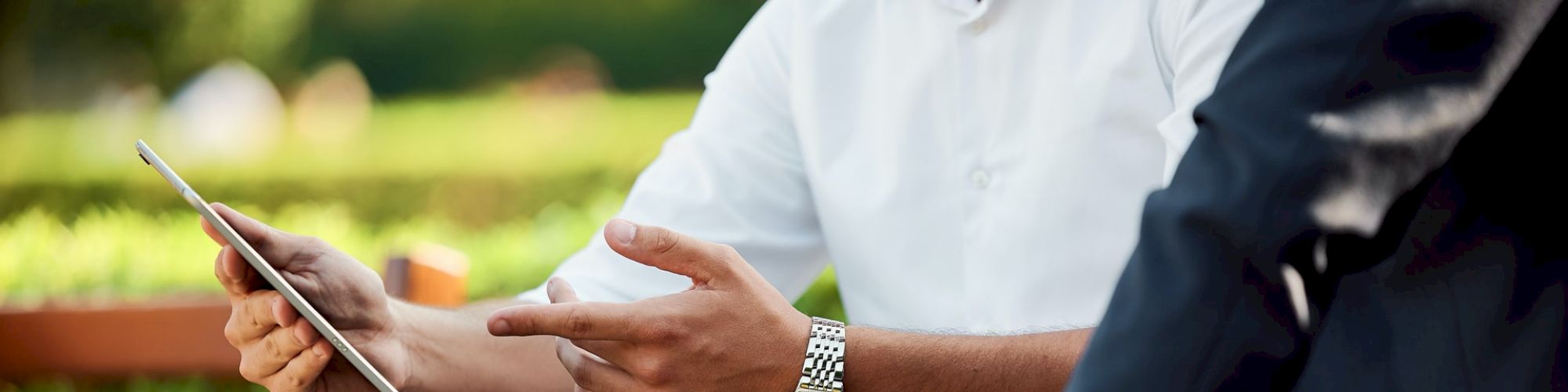 Two people sitting outside. One is holding a tablet, and both appear to be engaged in a discussion, possibly about business or a project.