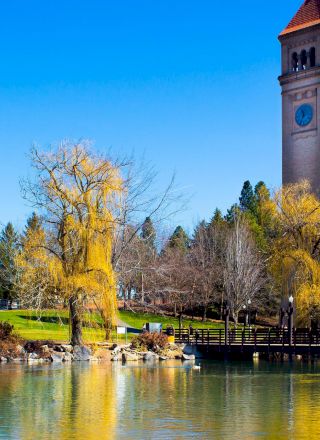 The image shows a picturesque scene with a tall clock tower, a pavilion-style structure, trees, and a reflection in a tranquil body of water, ending the sentence.