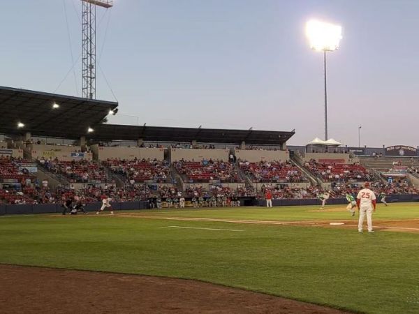 A baseball game is taking place at a well-lit stadium in the evening, with players on the field and a crowd watching from the stands.