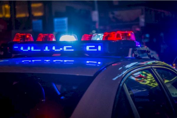 The image shows a police car with its red and blue lights flashing in the night, reflecting the word 