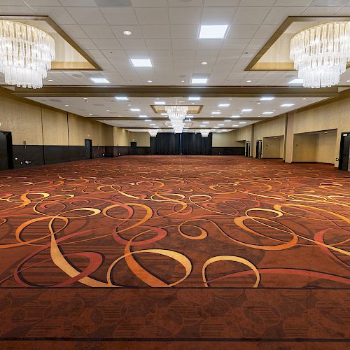 An empty, spacious ballroom with ornate chandeliers, patterned carpet, and beige walls, suitable for large events or gatherings.