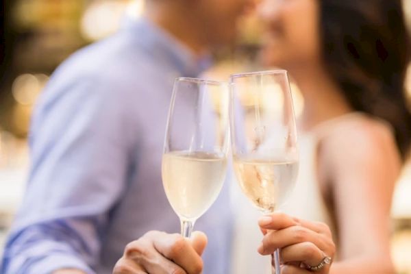 Two people clinking glasses of champagne in a toast, likely celebrating an occasion, with a blurred background creating an intimate atmosphere.