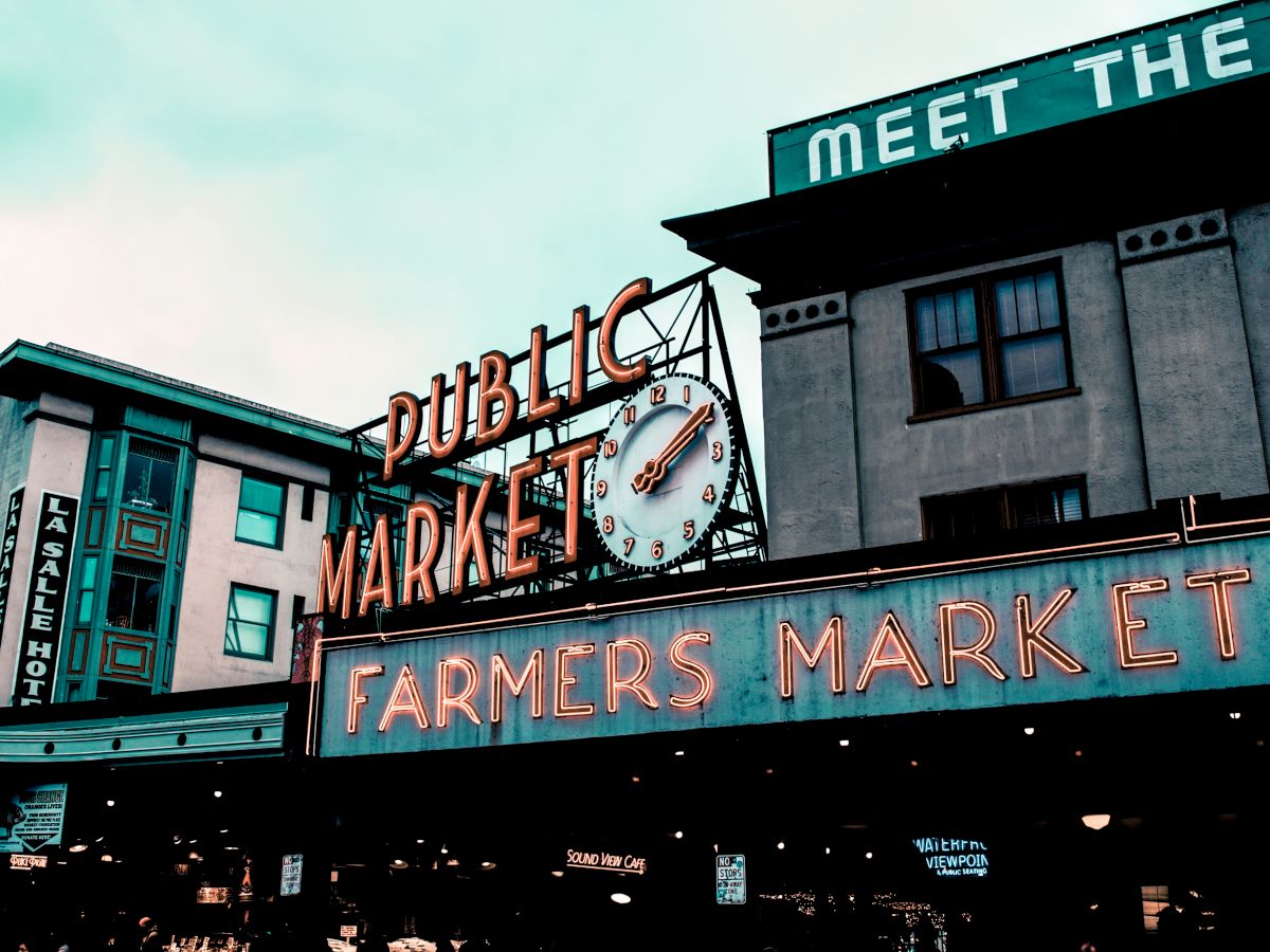 The image shows the "Public Market" and "Farmers Market" signage, with a large clock in the center, indicating an outdoor marketplace.