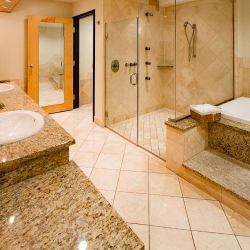 This image shows a spacious bathroom with granite countertops, a double sink, a walk-in shower with glass doors, and a large bathtub.