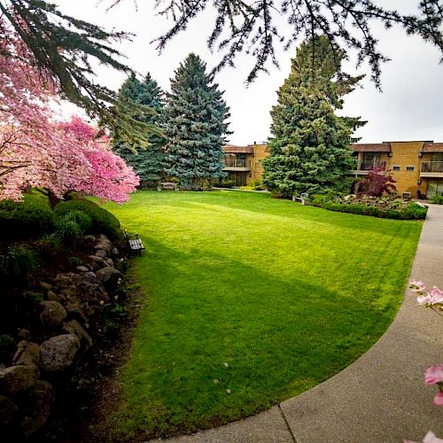 A well-maintained courtyard with green grass, pink blooming trees, and surrounding pathways leading to beige buildings, creating a serene ambiance.