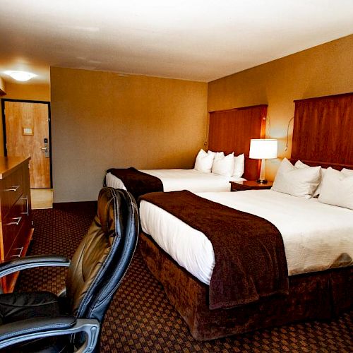 This image shows a hotel room with two double beds, a desk, a TV, an office chair, and a lamp. The room has a brown and beige color scheme.