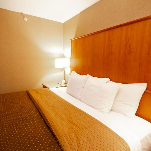 A neatly made bed with brown sheets and white pillows in a hotel room with a wooden headboard and a bedside lamp.