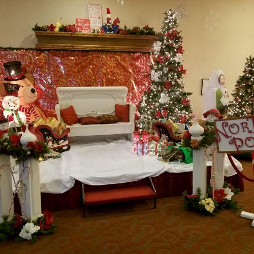 A festive holiday display with decorated Christmas trees, a small sleigh, and a sign that reads 